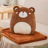A plush bear pillow sits on top of a folded orange travel blanket on a table.