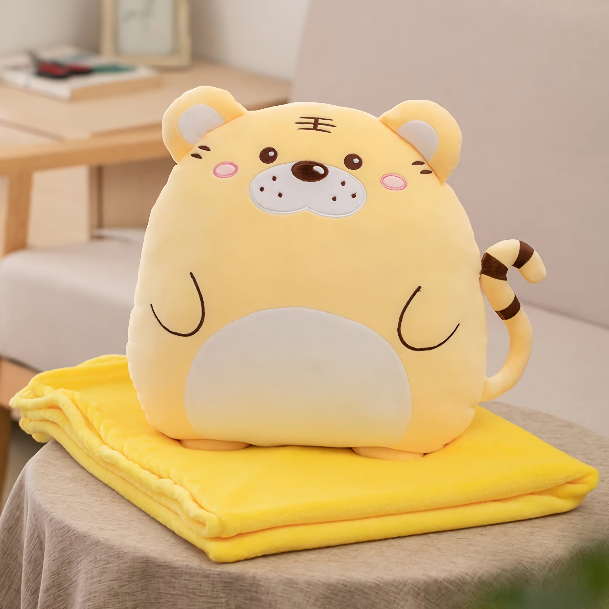 Yellow plush tiger pillow on a folded yellow blanket on a table.