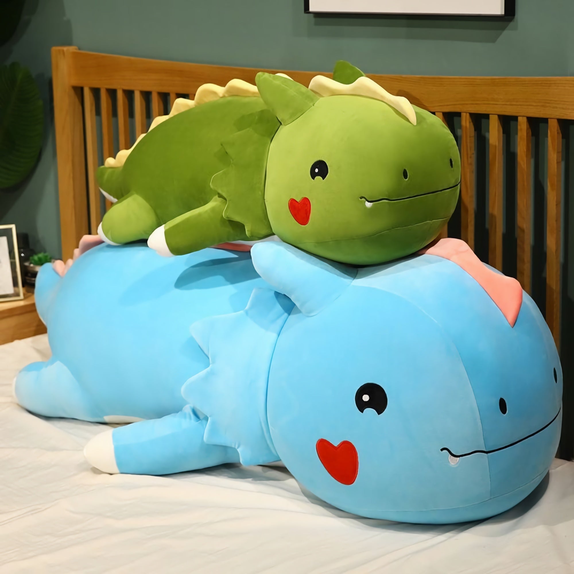A large blue dinosaur plush pillow with a smaller green dinosaur plush on top, both with cute facial features.