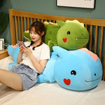 A person sits on a bed with large plush dinosaur pillows, using a phone and smiling.