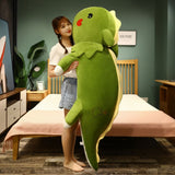 A person holds a large green dinosaur plush pillow in a bedroom setting.