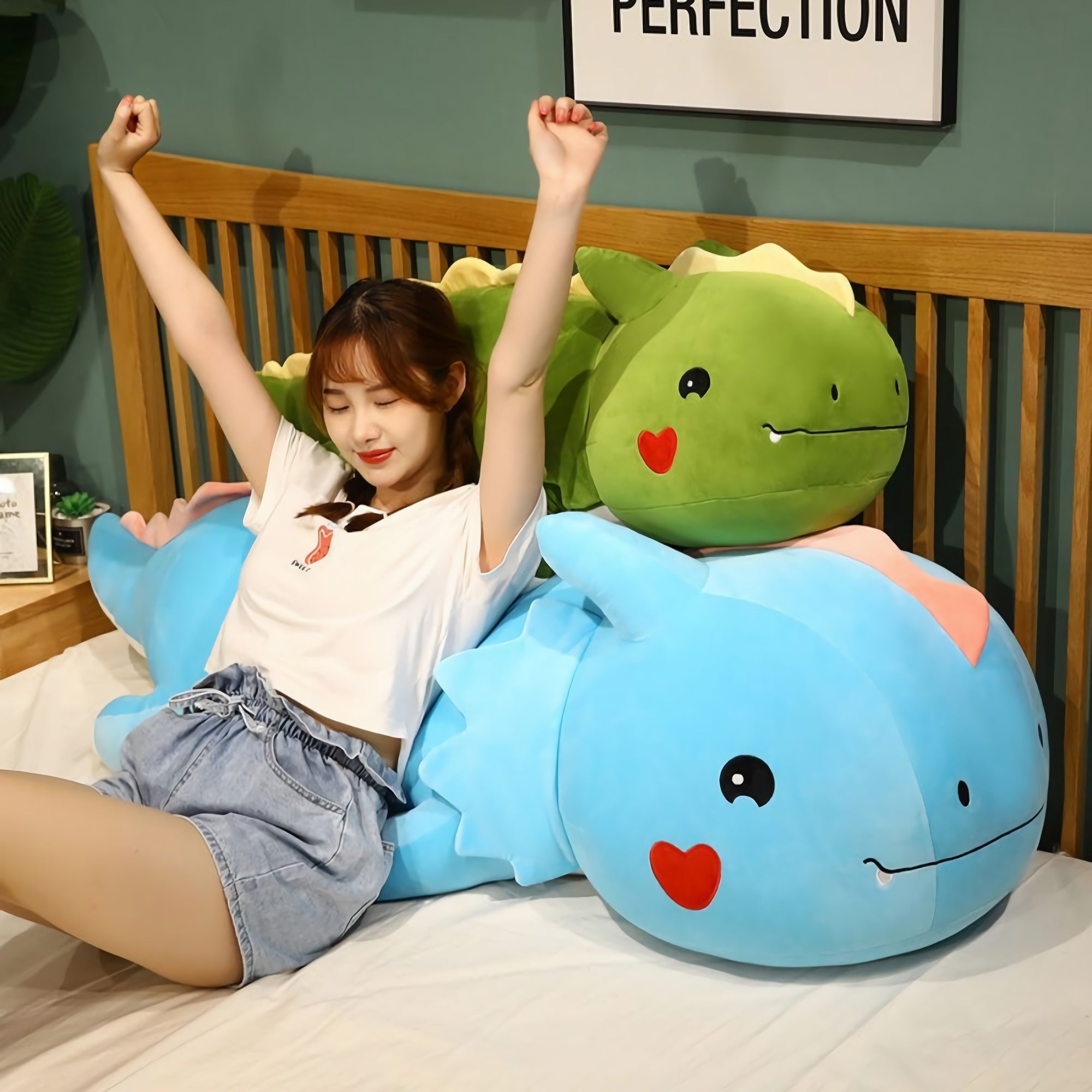 A person sits on a bed with two large, colorful dinosaur plush pillows, stretching and smiling.