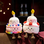 Two plush cake pillows with candles, colorful decorations, and smiling faces, sitting on a couch.