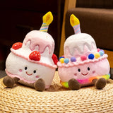 Two cute plush cake pillows with candles, smiling faces, and colorful decorations, sitting on a woven mat.
