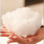 A person holding a fluffy, white pillow filling in their hands.