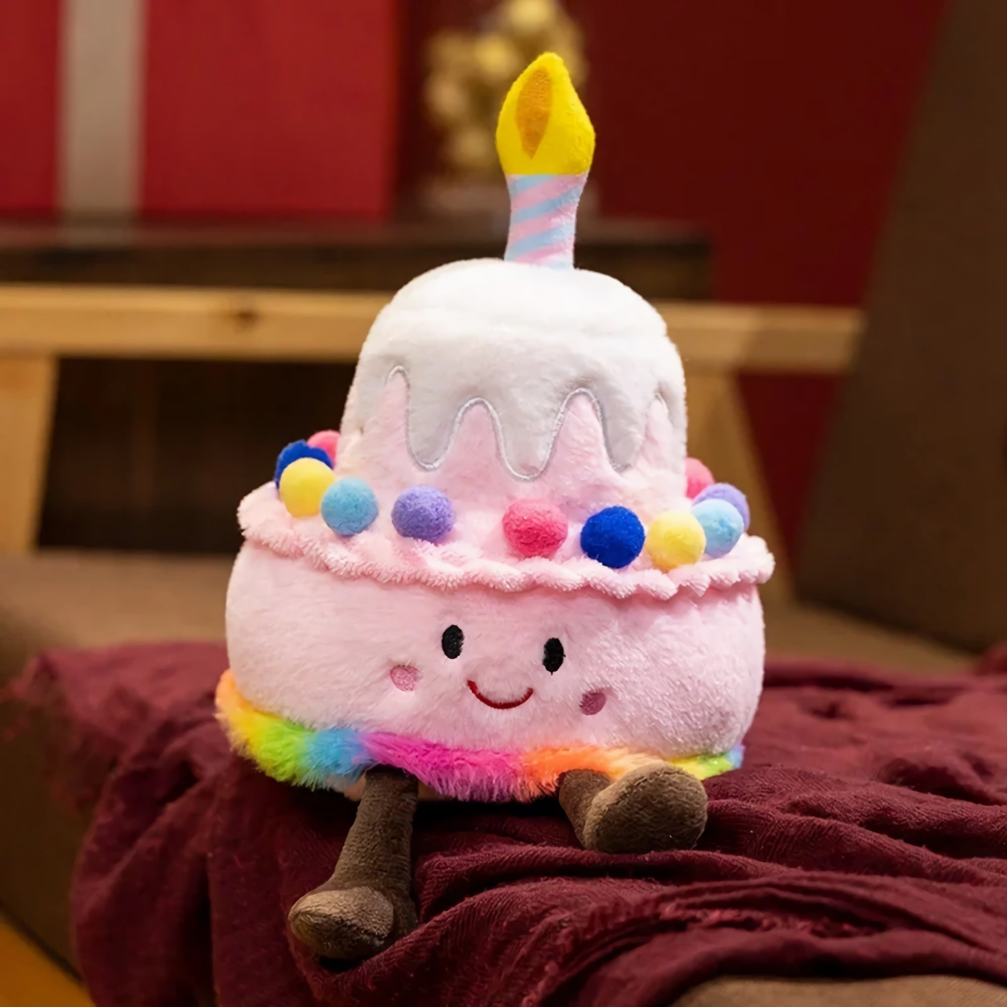 Kawaii plush pillow shaped like a birthday cake with a candle, colorful pom-poms, and a smiling face.