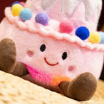 Kawaii plush pillow shaped like a birthday cake with a smiling face and colorful pom-poms on top.