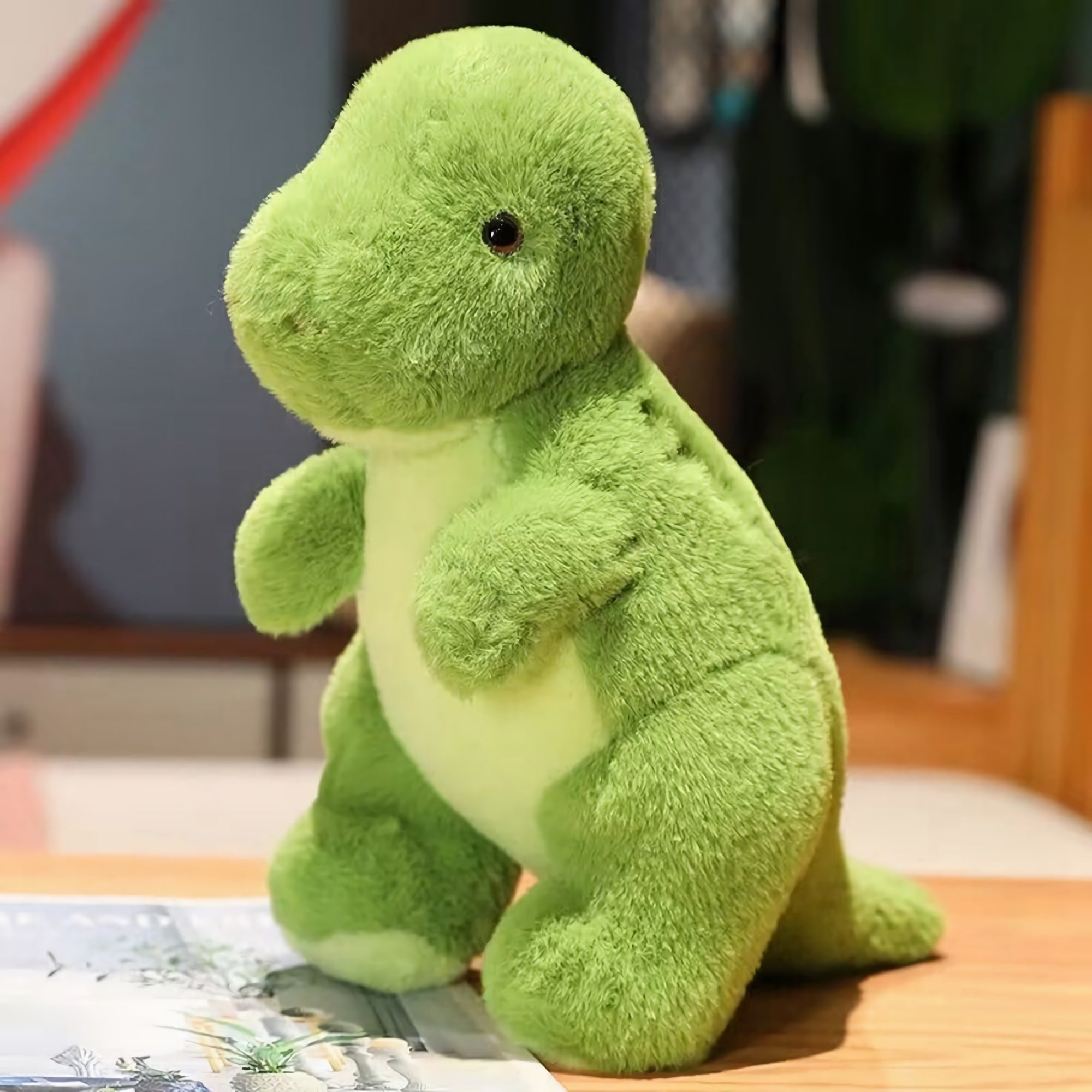 Green plush dinosaur toy with a rounded head and small arms, standing on a wooden surface.