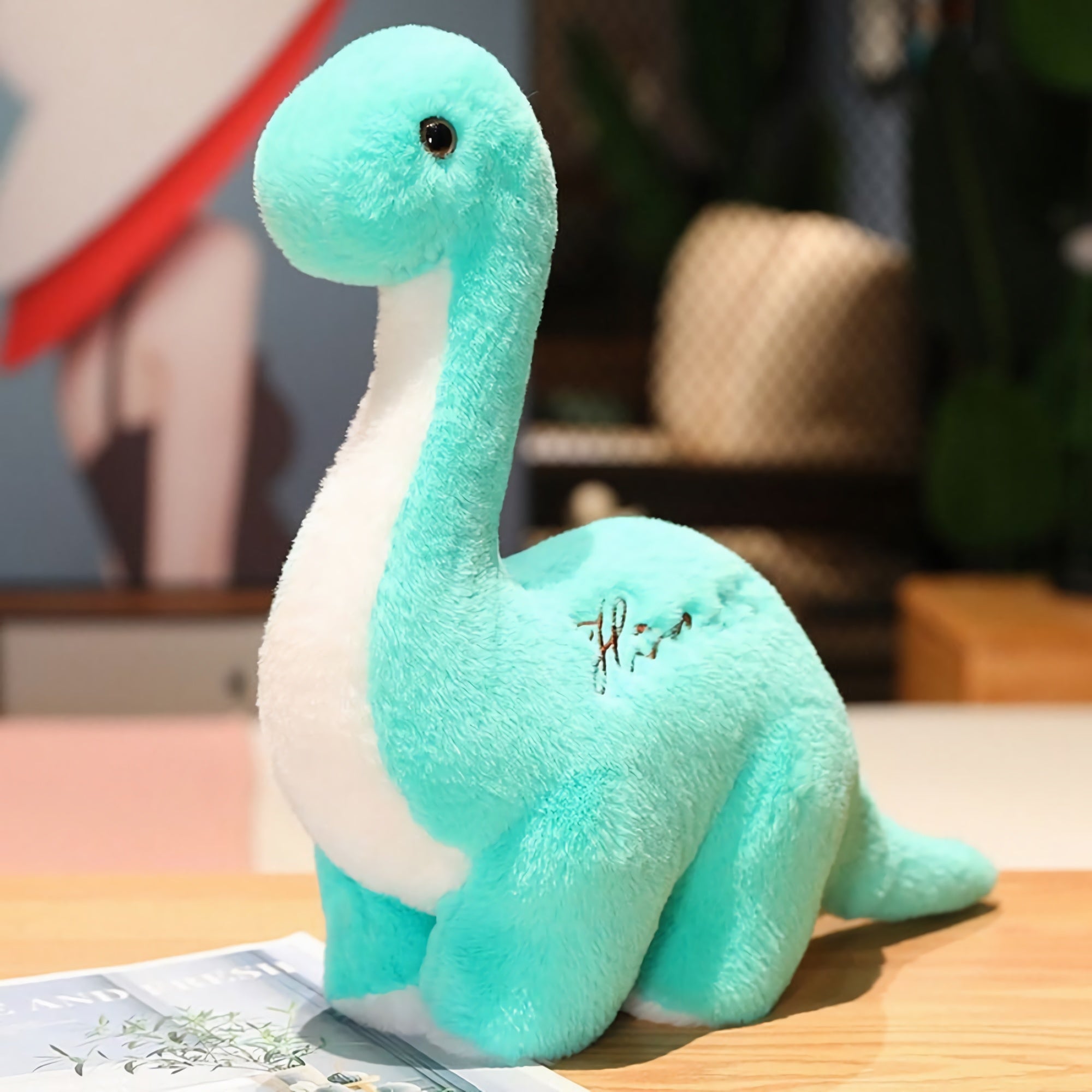 A soft, turquoise dinosaur plush toy with a white belly, sitting on a wooden surface.