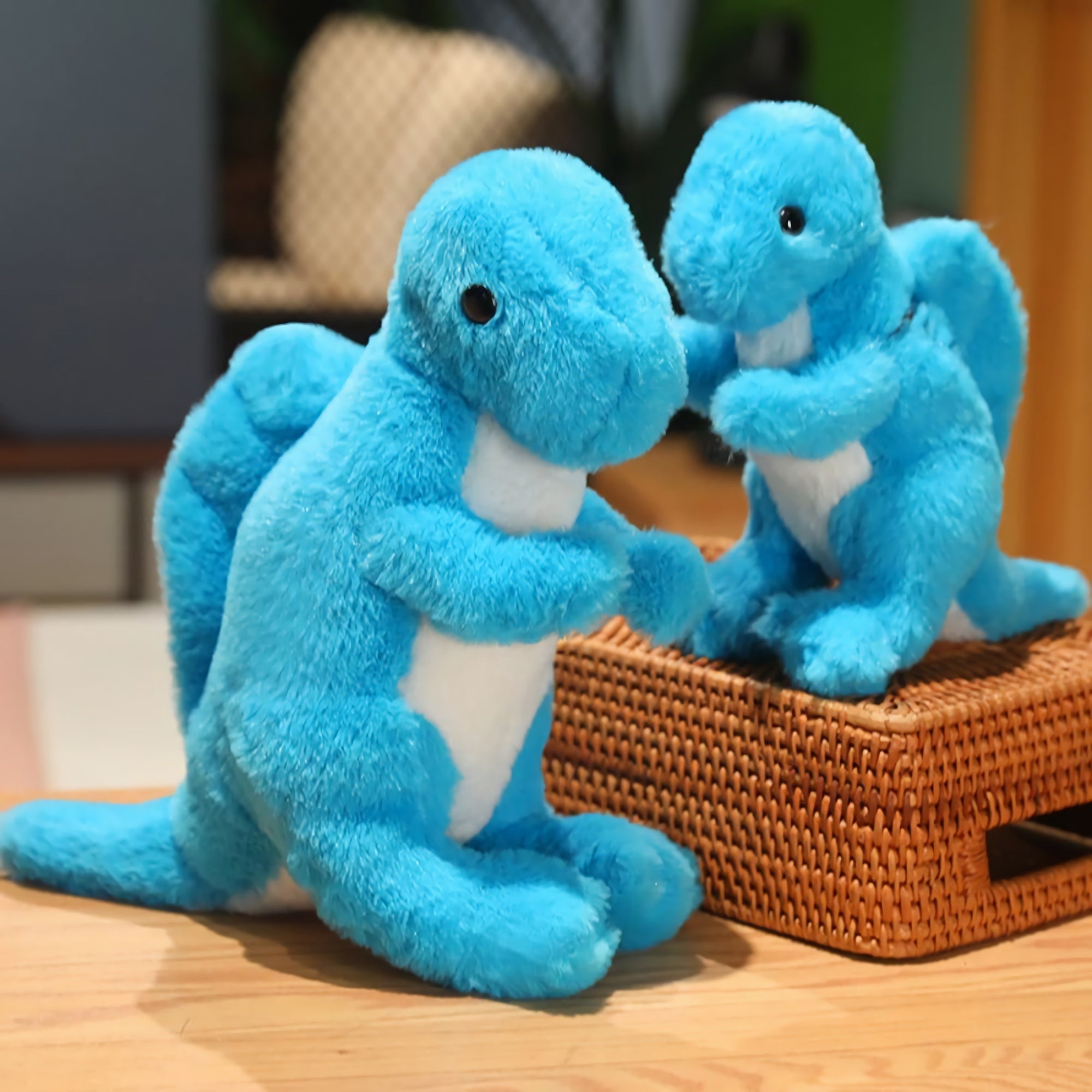 Two blue plush dinosaur toys with white bellies, one larger and one smaller, sitting on a woven basket.