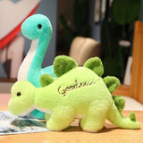 Two plush dinosaur toys, one blue and one green, displayed on a wooden surface with a magazine nearby.