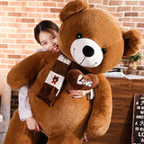 A person hugs a large brown teddy bear plush with a scarf and a heart-shaped "Love" patch.