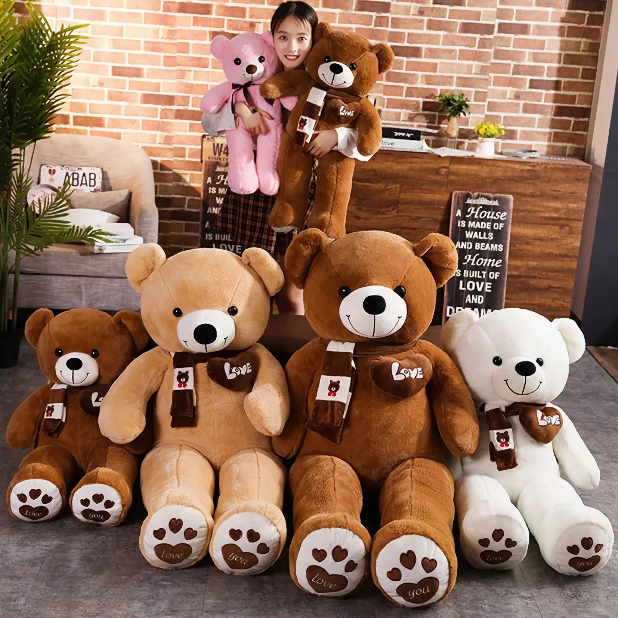 A girl holds a pink teddy bear while standing among several large teddy bears in different colors and sizes.