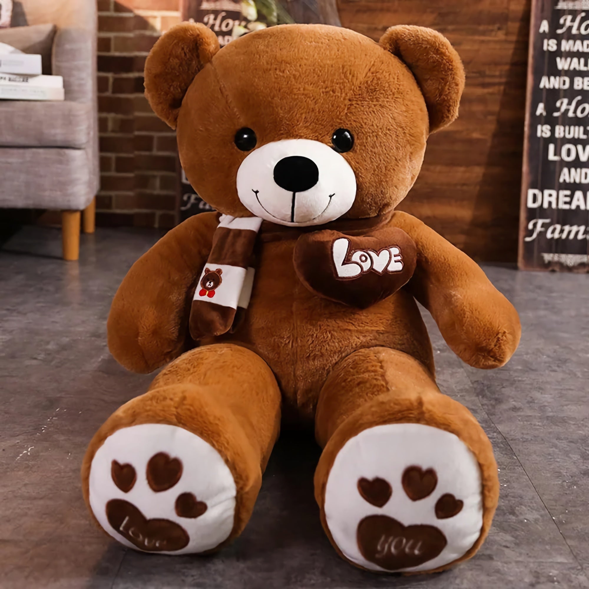 Brown teddy bear plush with a scarf, heart patch, and paw prints, sitting on a gray floor in a cozy room setting.