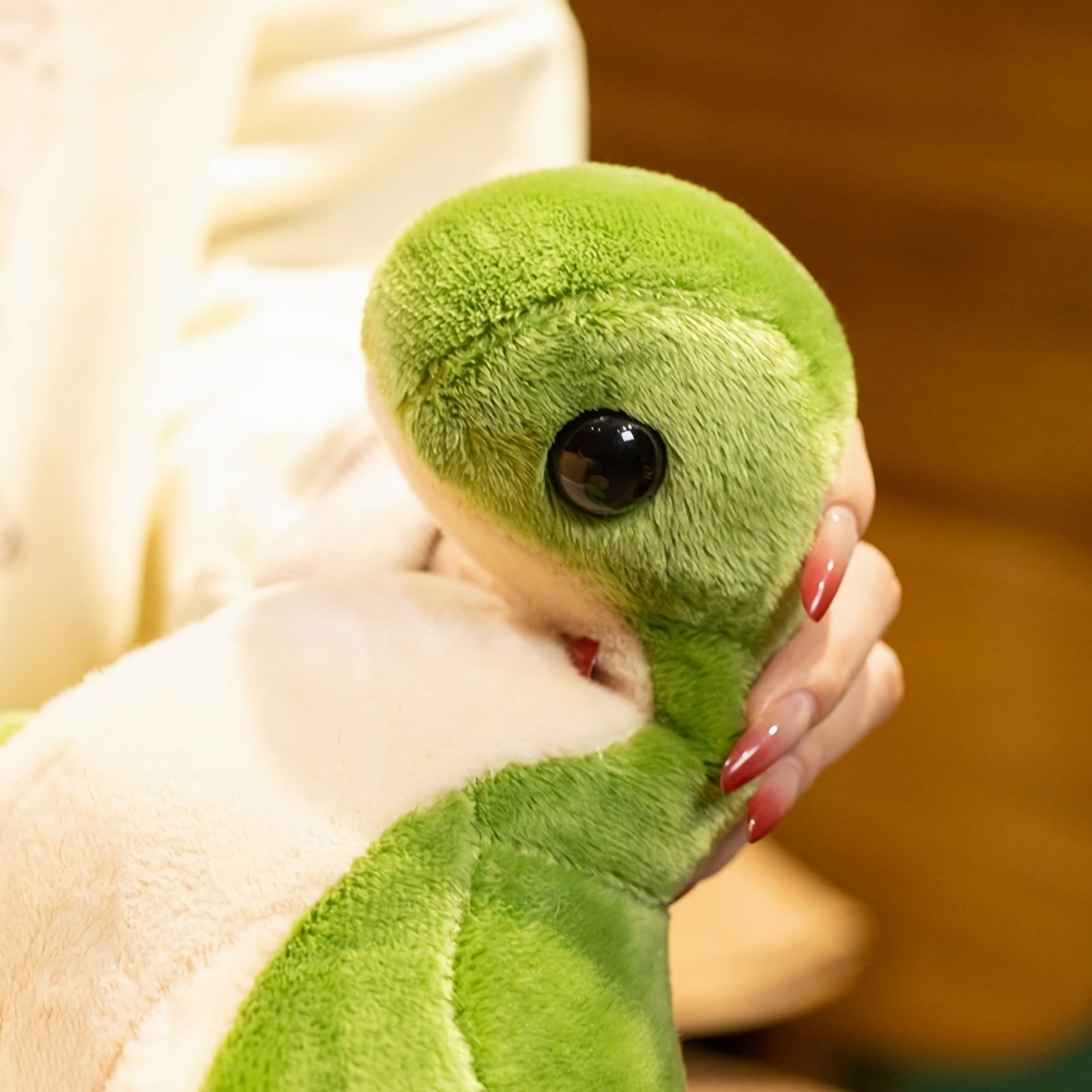 A close-up of a green plush dinosaur with large eyes, being held by a person with long nails.