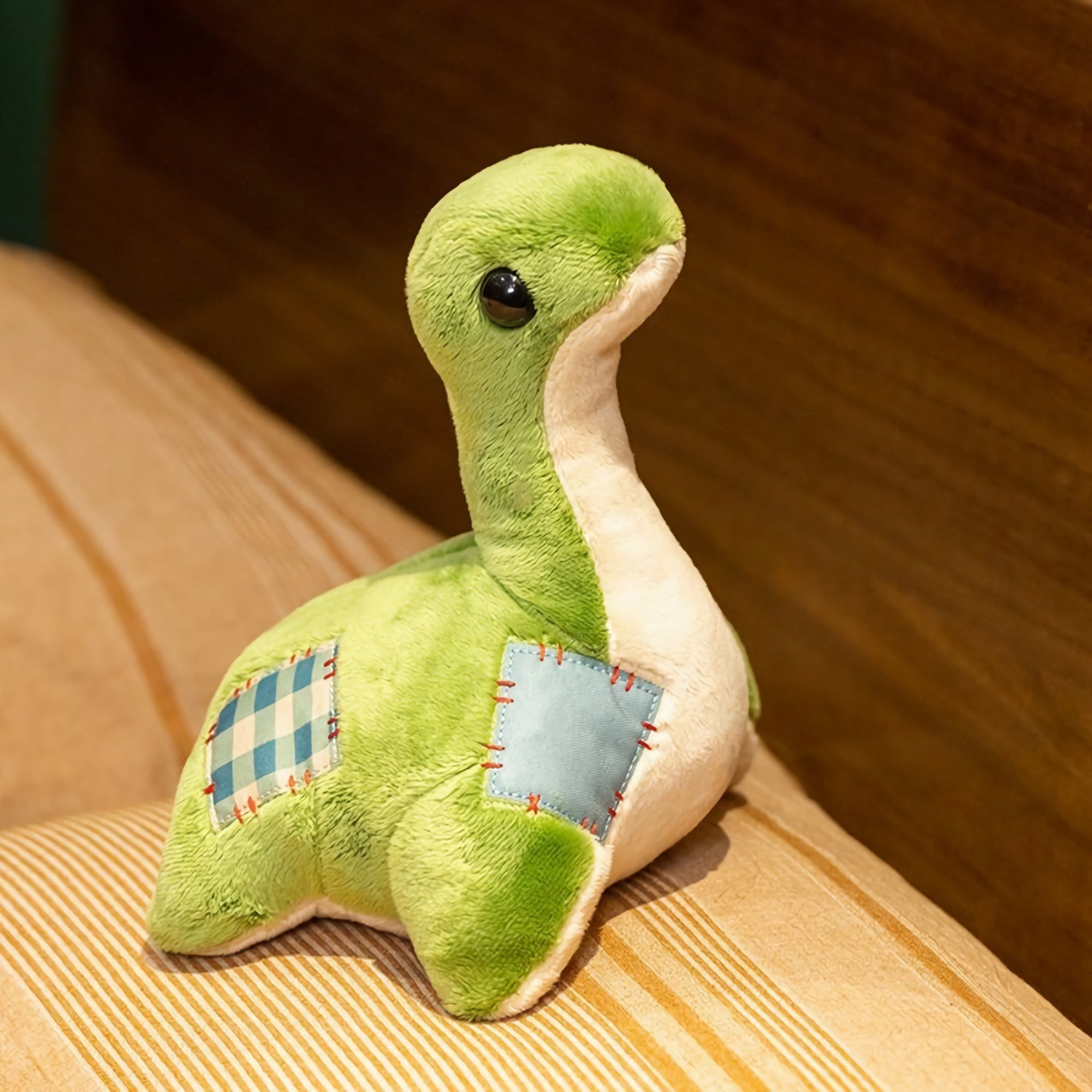 Green plush dinosaur with a long neck and patchwork details, sitting on a striped surface.