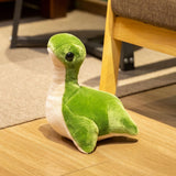 Plush toy resembling a Loch Ness monster, featuring green and white colors, sitting on a wooden floor.