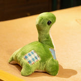 Green plush dinosaur with a long neck and stitched patches on its back, sitting on a wooden surface.