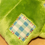 Close-up of a green plush toy with a stitched blue and white checkered patch.