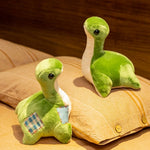 Two green plush dinosaur toys with black eyes, one with a patch, sitting on a pillow.