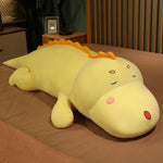 Long yellow dinosaur plush pillow with a smiling face, lying on a brown bedspread.