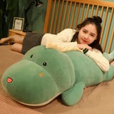 A person lies on a bed with a large green dinosaur plush pillow, smiling and resting on their arms.