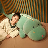 A girl sleeps beside a large, soft dinosaur-shaped plush pillow on a bed.