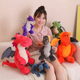 A person holding various colorful plush dragon and dinosaur toys while sitting on a couch.