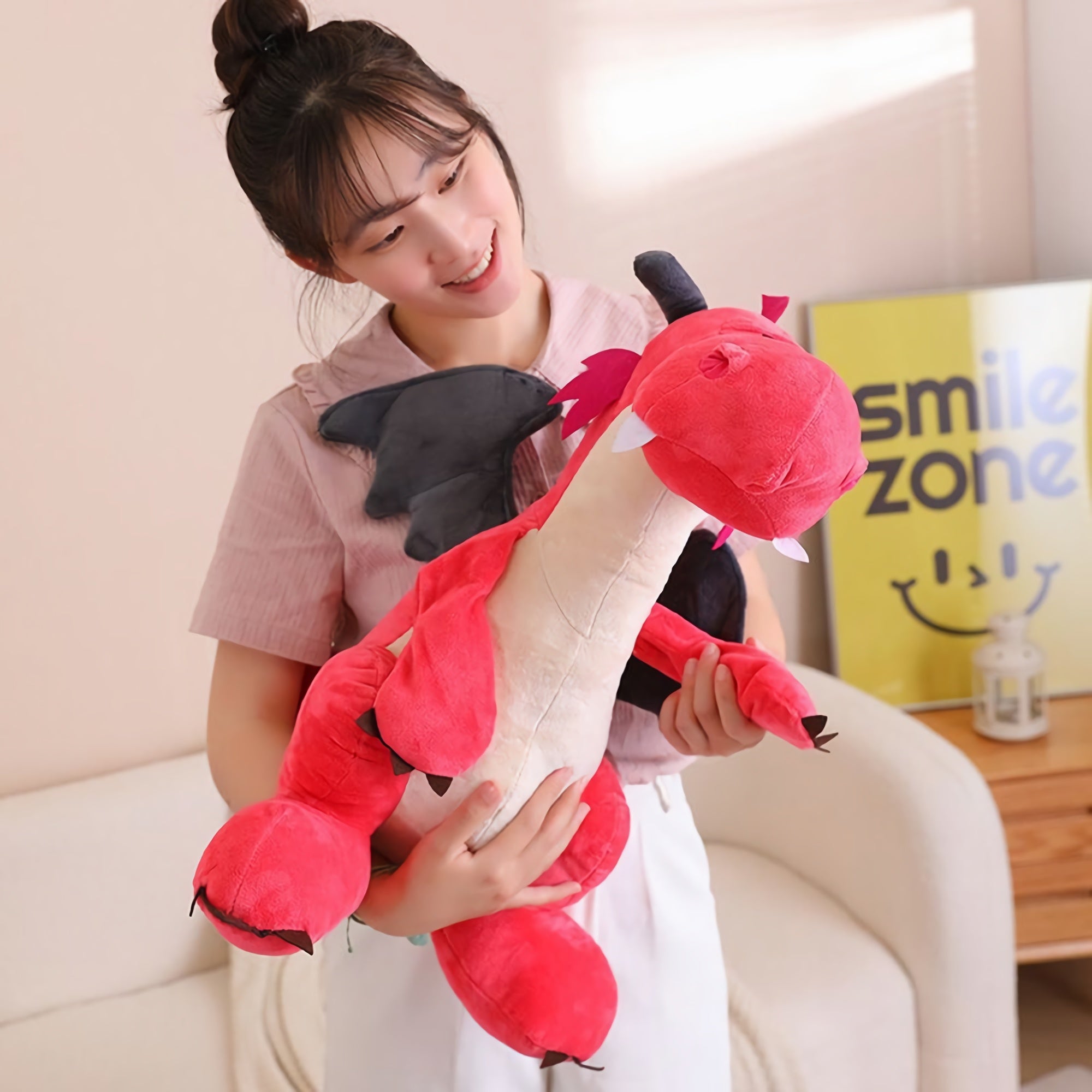A person holds a red plush dragon with black wings, smiling in a bright room.