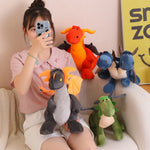 A person holds a plush dragon while surrounded by various colorful dragon and dinosaur plushies.
