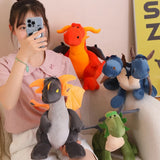 A person holds a plush dragon while surrounded by colorful plush dragons and dinosaurs on a couch.