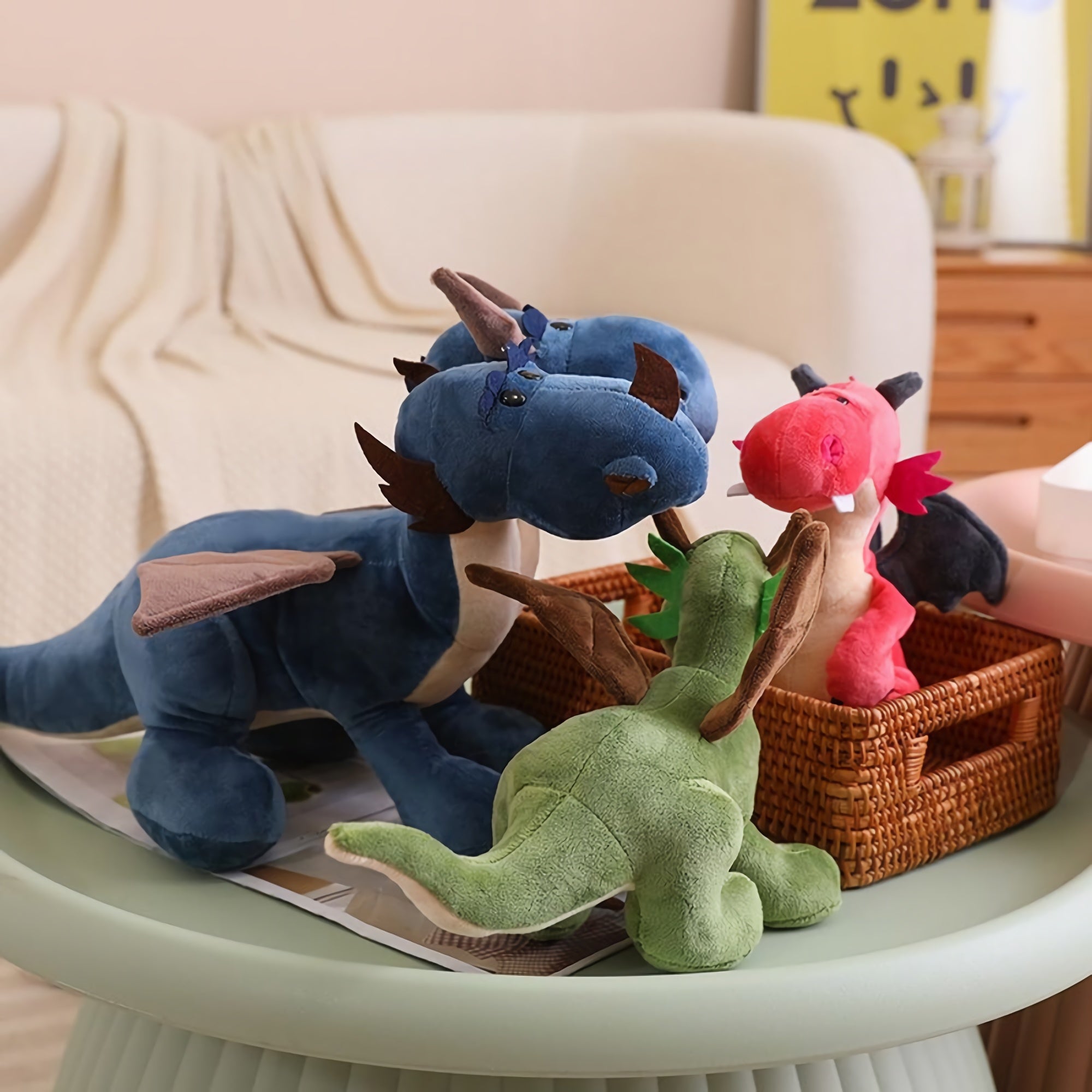 Three plush toys, including a blue dragon, green dinosaur, and pink dragon, on a table and in a woven basket.