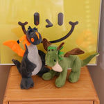 Two plush toys, a black and orange dragon and a green dinosaur with wings, on a wooden surface in front of a yellow poster.
