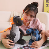 A person smiles while holding a plush dragon and a small dinosaur on a table with magazines.