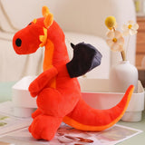 Red plush dragon with black wings sitting on a table near a vase with flowers.