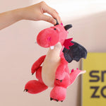 A person holds a red plush dragon with black wings and a beige belly against a light background.