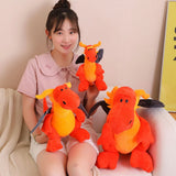 A person sitting on a couch holding three orange and yellow plush dragon toys with black wings.