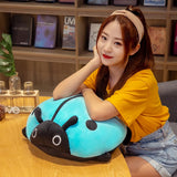 A person in a yellow shirt rests on a colorful ladybug plush pillow at a wooden table.