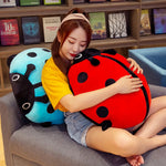 A person sits on a couch, hugging colorful ladybug plush pillows, one red and one blue, in a cozy setting.