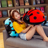 A woman sits on a couch holding a large red ladybug plush pillow, with a blue ladybug pillow behind her.