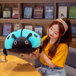 A woman in a yellow shirt holds a large, colorful ladybug plush pillow while sitting at a table.