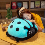 A person resting their head on a large, colorful ladybug-shaped plush pillow on a wooden table.