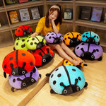 A person sits among colorful squishy ladybug plush pillows in a cozy indoor setting.