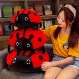A person sits beside three stacked red ladybug plush pillows with black spots and eyes.