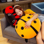 A person rests on colorful ladybug-shaped plush pillows while sitting on a couch.