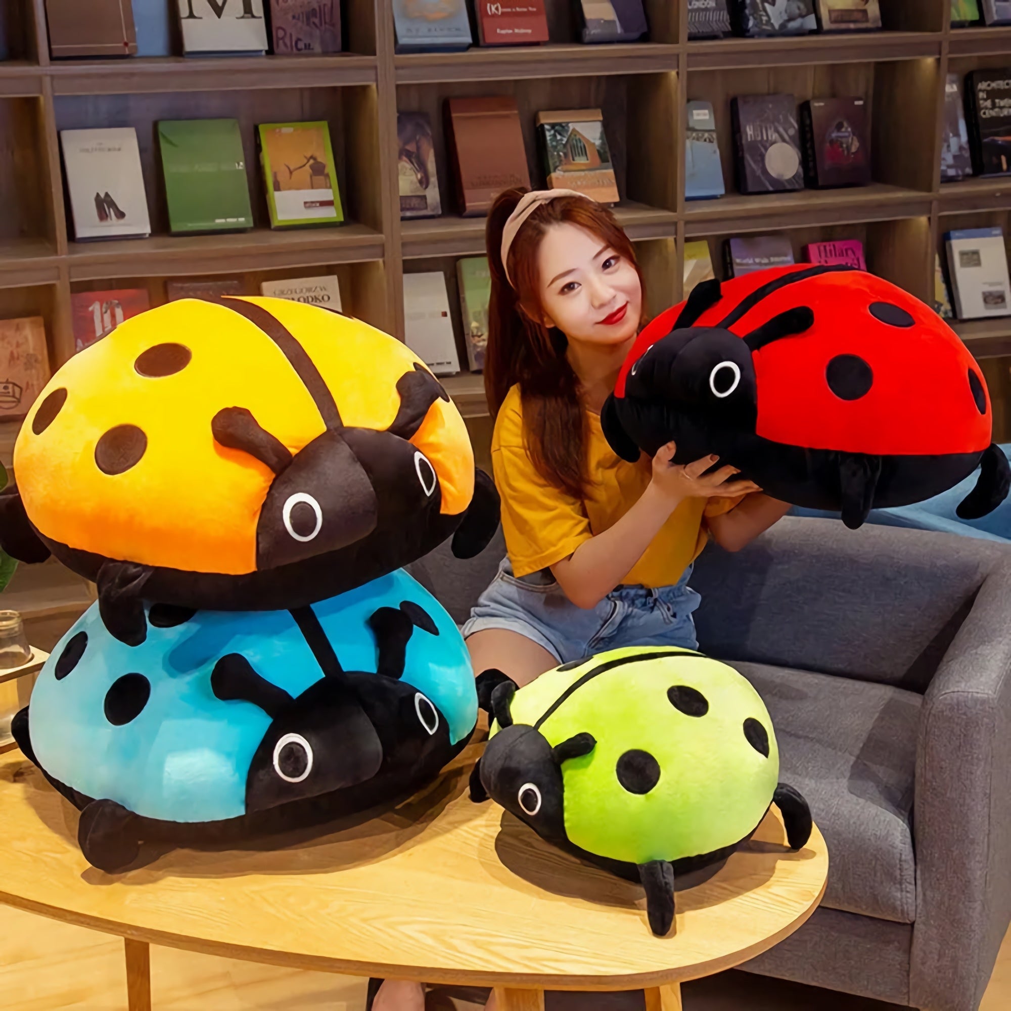 A person holds a red plush ladybug while colorful squishy ladybug pillows are stacked on a table.
