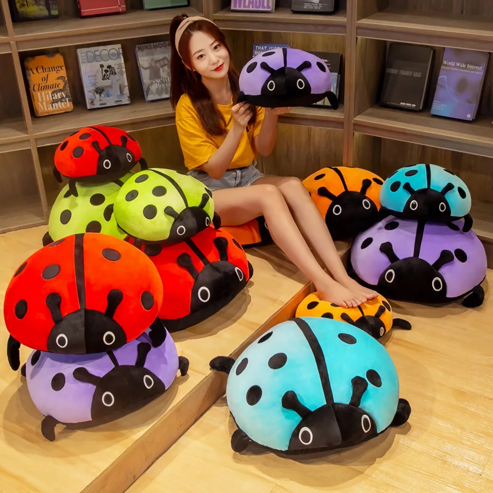 A person sits among colorful squishy ladybug plush pillows in various colors, smiling while holding one.