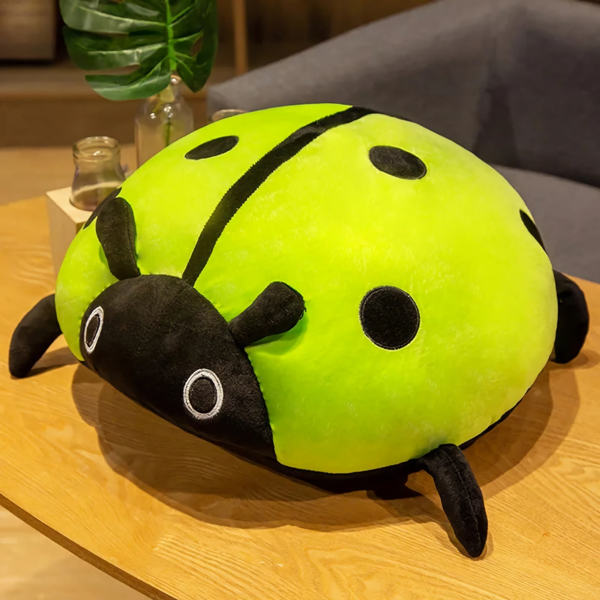 Colorful plush ladybug pillow with a green body, black spots, and black legs, resting on a wooden table.