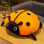Colorful plush ladybug pillow with orange body and black spots, resting on a wooden table.