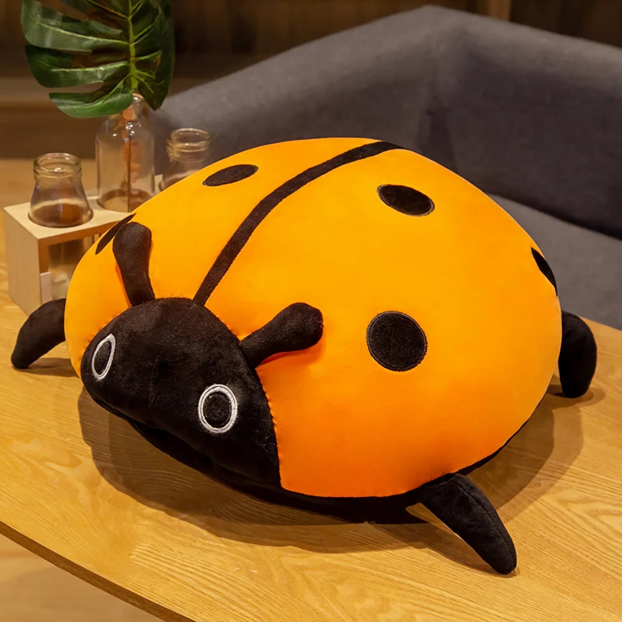 Colorful plush ladybug pillow with orange body and black spots, resting on a wooden table.